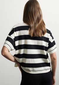 Maglietta a maniche corte, svasata, caratterizzata da audaci righe orizzontali bianche e nere, con una texture morbida e un orlo arrotondato.