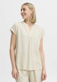 Blusa corta beige chiaro con maniche a sbuffo e scollo a V, realizzata in tessuto testurizzato. Presenta una vestibilità rilassata e dettagli di cucitura lungo il collo.