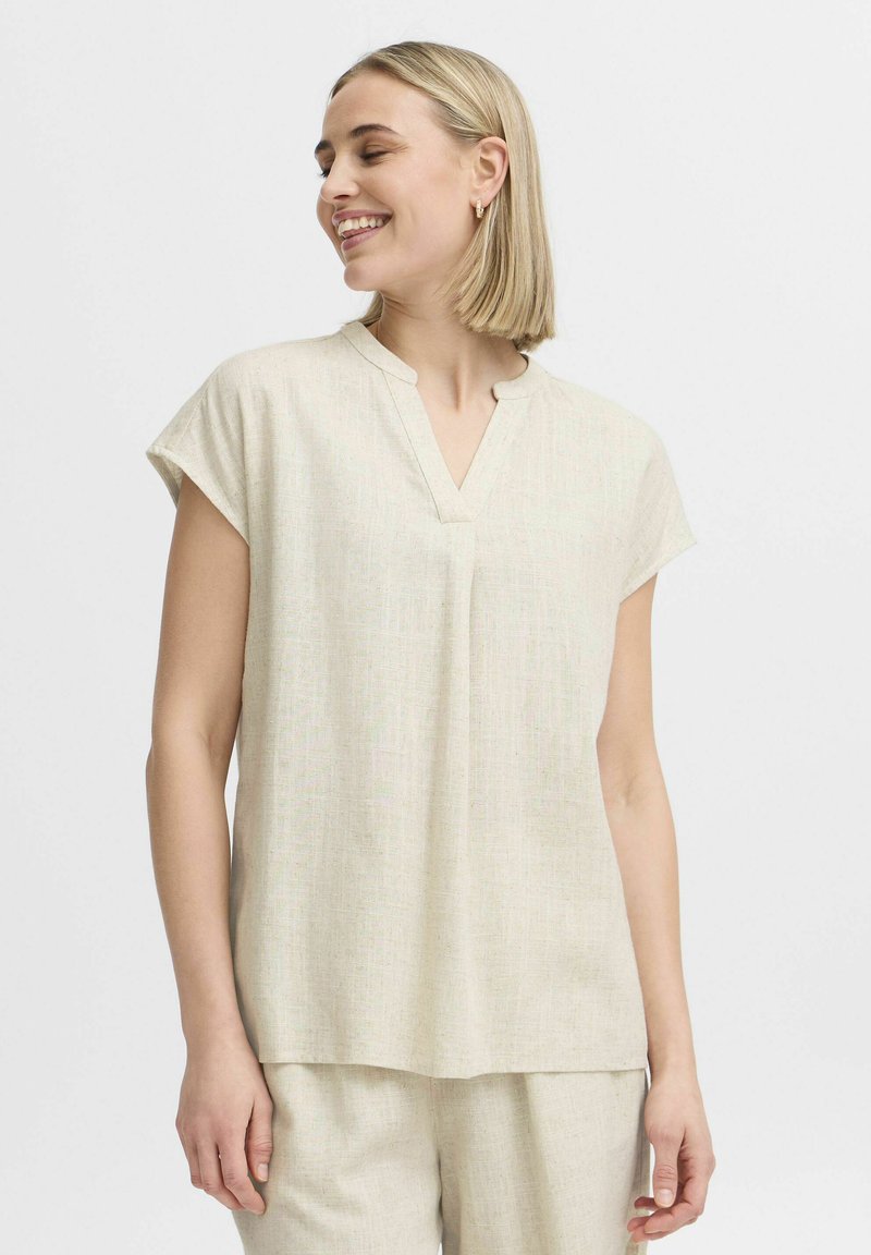 Blusa corta beige chiaro con maniche a sbuffo e scollo a V, realizzata in tessuto testurizzato. Presenta una vestibilità rilassata e dettagli di cucitura lungo il collo.