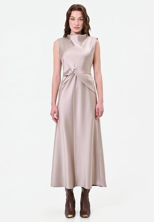Donna che indossa un abito midi in satin beige senza maniche con dettaglio nodo in vita e stivaletti marroni con punte dorate.