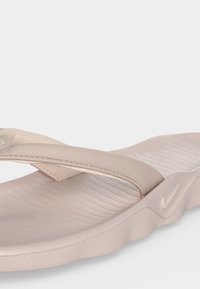 Μπεζ σανδάλι Nike flip-flop με υφή στο πέλμα, χοντρό μαξιλαρωτό λουράκι και μικρό λογότυπο Nike swoosh στο πλάι της σόλας.