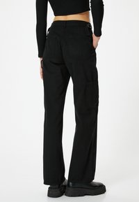 Pantaloni cargo neri con un taglio dritto, due tasche posteriori e una tasca laterale. Realizzati in un tessuto resistente con una texture morbida.