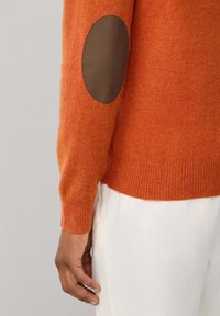Maglione arancione realizzato in materiale morbido, con toppe marroni ai gomiti, polsini e orlo a costine, dal design comodo e rilassato.
