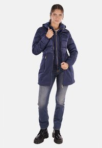 Cappotto puffer blu scuro con chiusura con zip, cappuccio e tasche laterali. Presenta una texture a costine sulle maniche e una finitura liscia sul corpo.