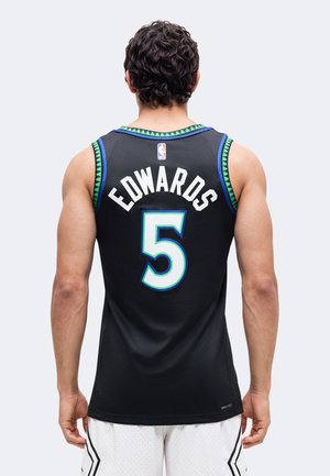 Homme aux cheveux bouclés foncés portant un maillot de basket noir avec le nom Edwards et le numéro 5, associé à un short blanc, debout de dos.