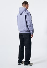 Ljuslila hoodie med stor huva, parat med svarta raka byxor. Outfitten har en avslappnad passform och en mjuk bomullstextur.