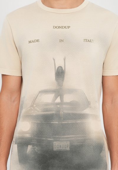 Beige bomulds t-shirt med et falmet gråt grafik, der viser en bil og en figur med hævede arme. Teksten læser "DONDU" og "MADE IN ITALY."