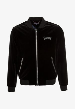 Chaqueta bomber de terciopelo negro con cierre de cremallera frontal, puños y dobladillo acanalados, bolsillos laterales y bordado "Tommy" en el pecho.