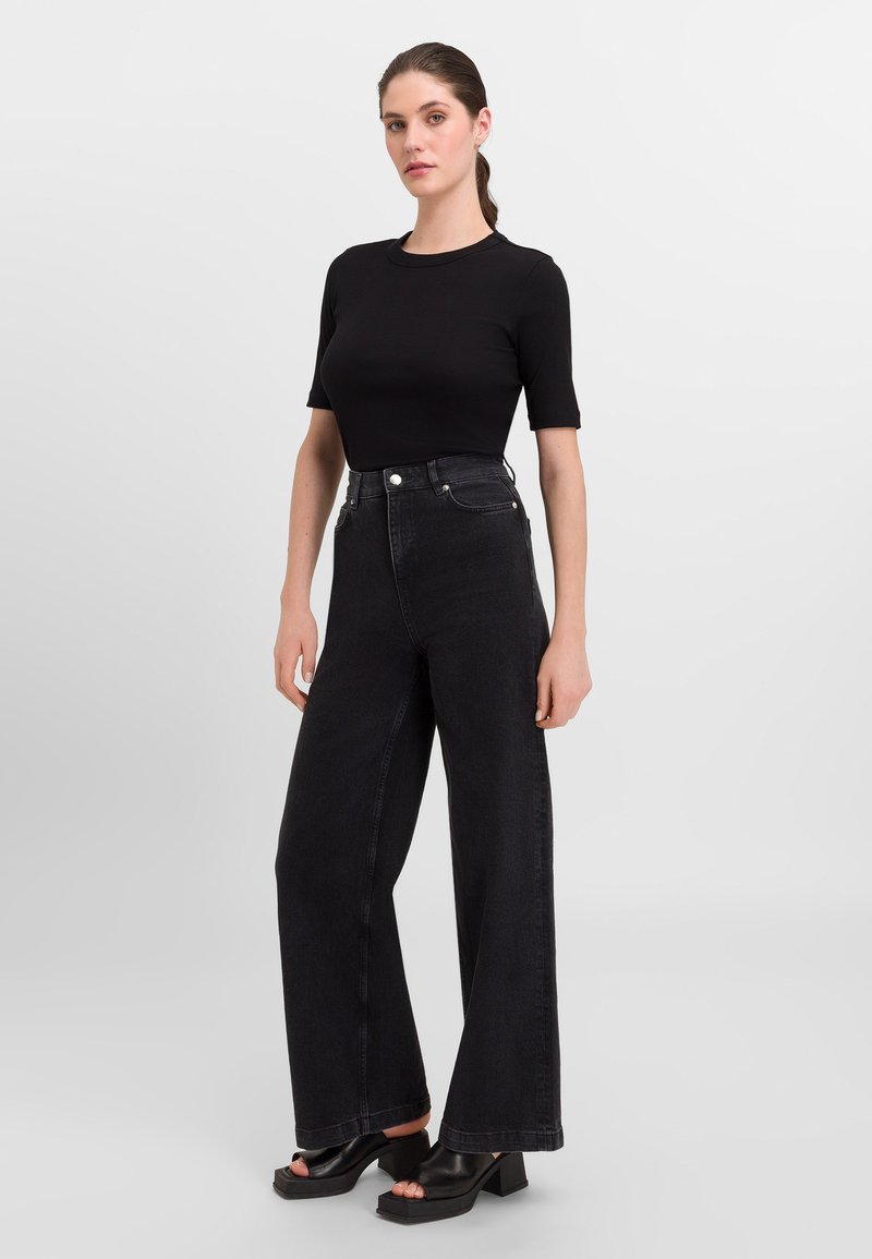Zwarte denim jeans met hoge taille en wijde benen, gecombineerd met een aansluitend zwart T-shirt met korte mouwen en chunky zwarte sleehakken.