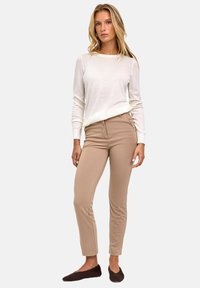 Beżowe dopasowane spodnie o gładkiej fakturze i subtelnym połysku, zestawione z lekkim, długim rękawem, kremową bluzką.