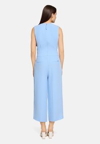 Combinaison bleu clair sans manches avec un corsage ajusté et un pantalon à jambes larges, dotée d'une fermeture éclair à l'arrière et de deux poches arrière.