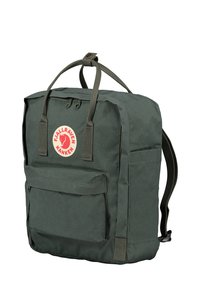 Sac à dos vert foncé avec des bretelles rembourrées, une poche avant et un logo circulaire distinctif. Fabriqué en tissu durable avec un design simple.
