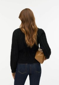 Czarny, teksturowany sweter z prążkowanymi rękawami i dopasowaną talią, zestawiony z ciemnym dżinsem i beżową kopertówką.