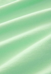 Tessuto di cotone verde chiaro con una superficie liscia, caratterizzato da dolci onde e pieghe che creano morbide ombre e riflessi.