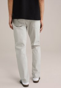 Lichtgrijze katoenbroek met een rechte snit, vijf zakken en zichtbare stikseldetails, gedragen met witte schoenen en een zwart shirt.