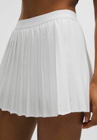 Close-up of a person wearing a white pleated skirt, showing the skirt's waistband and texture with part of the arm visible.