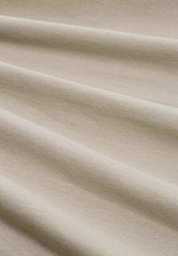 Tela de algodón beige claro con una textura suave, que presenta suaves ondulaciones y pliegues, creando un aspecto blando y acogedor.