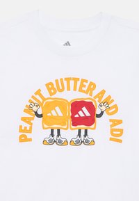 Hvit T-skjorte med et tegneserieillustrasjon av karakterer av peanøttsmør og gelé, med oransje og røde accenter og fet, lekende typografi.