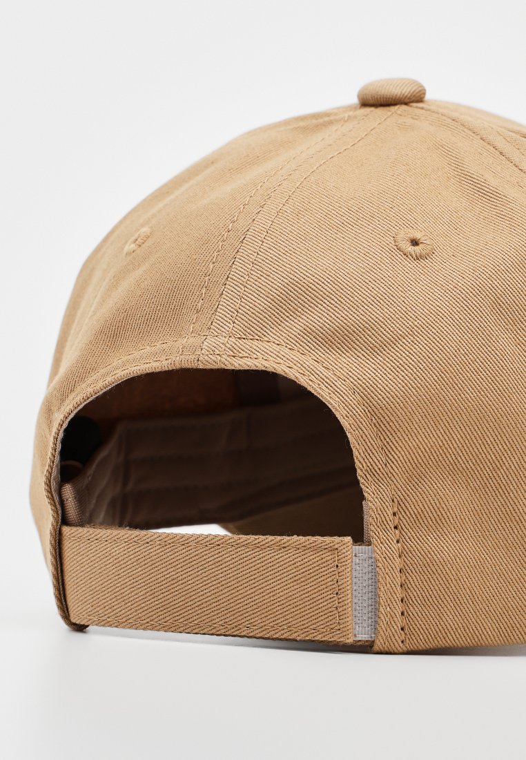 Casquette de baseball beige avec un extérieur en tissu doux, des coutures contrastées et une sangle ajustable à l'arrière. Design structuré avec des trous de ventilation.