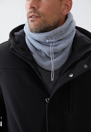 Hellgrauer Fleece-Schlupfschal mit Kordelzugdetail, darüber getragen eine dunkle Jacke mit Reißverschluss und silbernen Akzenten. Saubere, strukturierte Oberfläche.