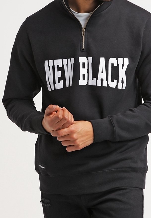 Sweat-shirt noir avec col à fermeture zippée partielle, arborant un texte blanc audacieux "NEW BLACK" sur la poitrine. Poignets et ourlet côtelés avec détail logo.