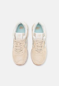 Beige tenisky New Balance 574 s svrchním dílem z kvalitní semišové kůže, perforovanými detaily, světlými modrými vložkami a bílými akcenty na jazyku a logu.