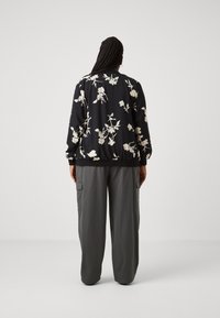 Svart bomberjacka med vitt blommönster, resår vid mudd och kant, kombinerad med lösa, grå cargobyxor med sidofickor.