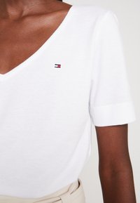 Biały t-shirt z krótkim rękawem w kształcie litery V, wykonany z bawełny, z małym logo w kolorach czerwonym, białym i niebieskim na lewej piersi.