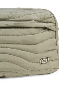 Bolso acolchado en verde oliva con un patrón texturizado en forma de olas. Presenta un logo plateado y costuras sutiles, con cierre de cremallera.