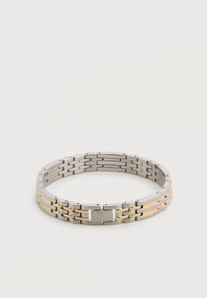 Bracelet en métal argenté et doré avec un fermoir rectangulaire gravé du nom d'une marque sur fond blanc.
