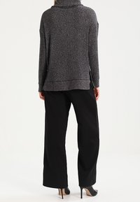 Šedý žebrovaný svetr s vysokým límcem, spárovaný s volnými černými kalhotami a černými vysokými podpatky, viděný ze zadní strany.