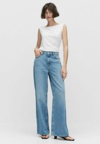 Haut sans manches blanc associé à un jean taille haute bleu clair et à jambes larges. La tenue présente un design décontracté et une texture de tissu lisse.