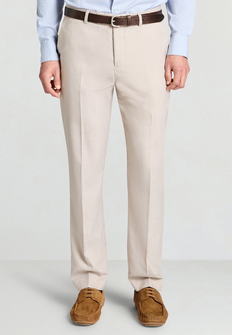Pantaloni beige su misura in tessuto strutturato, con parte anteriore liscia, gambe dritte e cintura in pelle marrone; abbinati a scarpe in camoscio marrone.