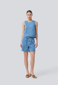Denim sleeveless top and matching shorts in light blue, featuring a relaxed fit, drawstring waist, and casual design. Brown heeled sandals complete the look.