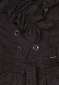 Svart dubbelknäppt kavaj med rynkad krage, försedd med svarta knappar, midjebälte och slät textur.