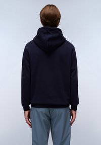 Marineblauwe hoodie van zachte stof, met een grote capuchon, geribbelde manchetten en een relaxte pasvorm. Draag het met lichtgrijze broeken.