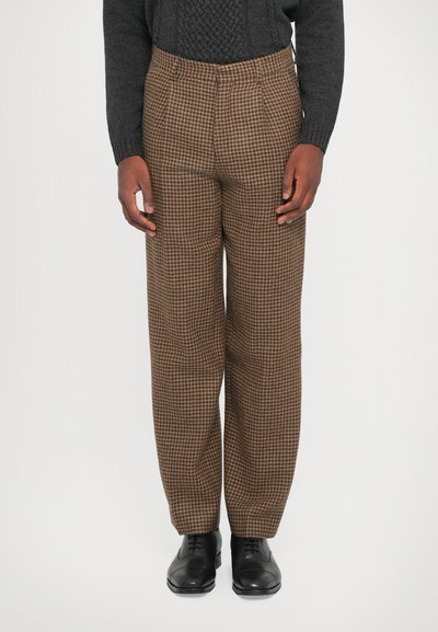 Barna houndstooth mintázatú, lazán szabott nadrág, rugalmas derékkal, elülső redőkkel, fekete cipőkkel párosítva.