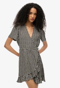 Vestido envolvente negro y crema con mangas cortas, escote en V profundo, tela suave y un dobladillo con volantes que presenta un patrón geométrico.
