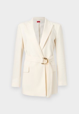 Blazer sur mesure couleur crème avec manches longues, larges revers, poches à rabat avant et ceinture assortie avec une boucle double anneau dorée.