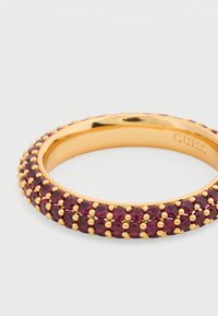 Δαχτυλίδι σε χρυσή απόχρωση με πολλαπλές σειρές στρογγυλών, βαθιά κόκκινων πολύτιμων λίθων σε λεία μπάντα, διακοσμημένο με χρυσές χάντρες κατά μήκος των άκρων.