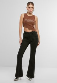 Brun ribbade crop top med vågig nederkant och silverdetaljer, kombinerad med svarta utsvängda jeans och högklackade skor i silver.