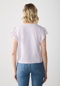 Top lila cu manșete scurte și transparente, cu volane. Material moale cu un design scurt. Asortat cu blugi albaștri cu talie înaltă.