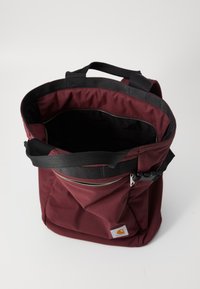 Burgunderfarget totebag med to svarte stropper, åpning på toppen og utvendig glidelåslomme. Glatt, slitesterk materiale med et romslig interiør.