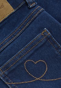 Jeans in denim blu scuro con cuciture marrone dorato e un motivo a cuore sulla tasca posteriore. Tessuto testurizzato con un design classico.