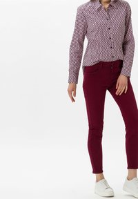 Chemise à manches longues bordeaux et blanche à motifs, devant boutonné, associée à un jean slim bordeaux et des baskets blanches. Tissu lisse et structuré.