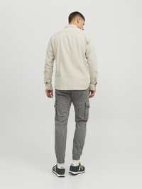 Light beige long-sleeve shirt with a buttoned collar, paired with gray cargo pants featuring side pockets and elastic cuffs, worn with green sneakers.