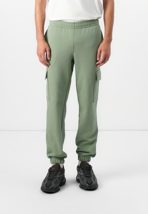 Green sweatpants with elastic cuffs, side pockets, and cargo pocket detail. Made from soft fabric, providing a relaxed fit and comfort.