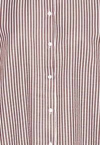 Button-up shirt featuring alternating burgundy and white vertical stripes. Made of lightweight fabric with a textured finish and white buttons.