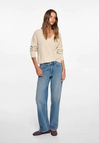 Beige randig tröja med V-ringning, tillsammans med ljusblå avslappnade jeans. Platta skor med ett strukturerat mönster fulländar outfiten.