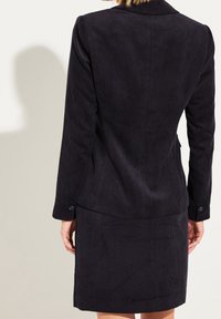 Laivastonsininen corduroy-takki, jossa on muotoiltu malli, hienovarainen kaitaleinen pinta, yksittäinen napitus ja yhteensopiva hame.